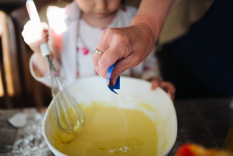 Grandma pours sugar into the dough with grandchild