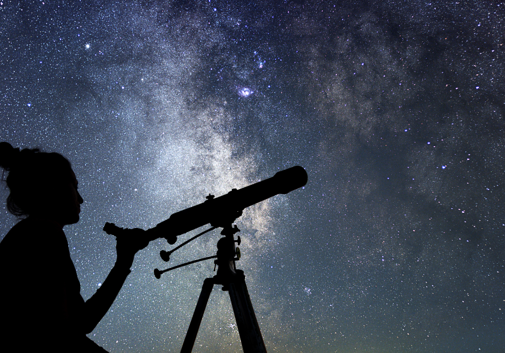 Silhouette of a person and telescope with the stars in the background